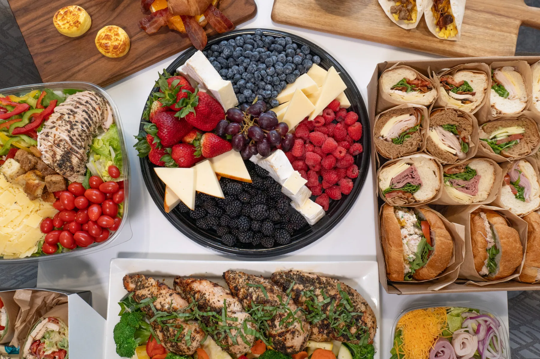 An overhead spread of catering trays, boxed sandwiches, salads and fruit